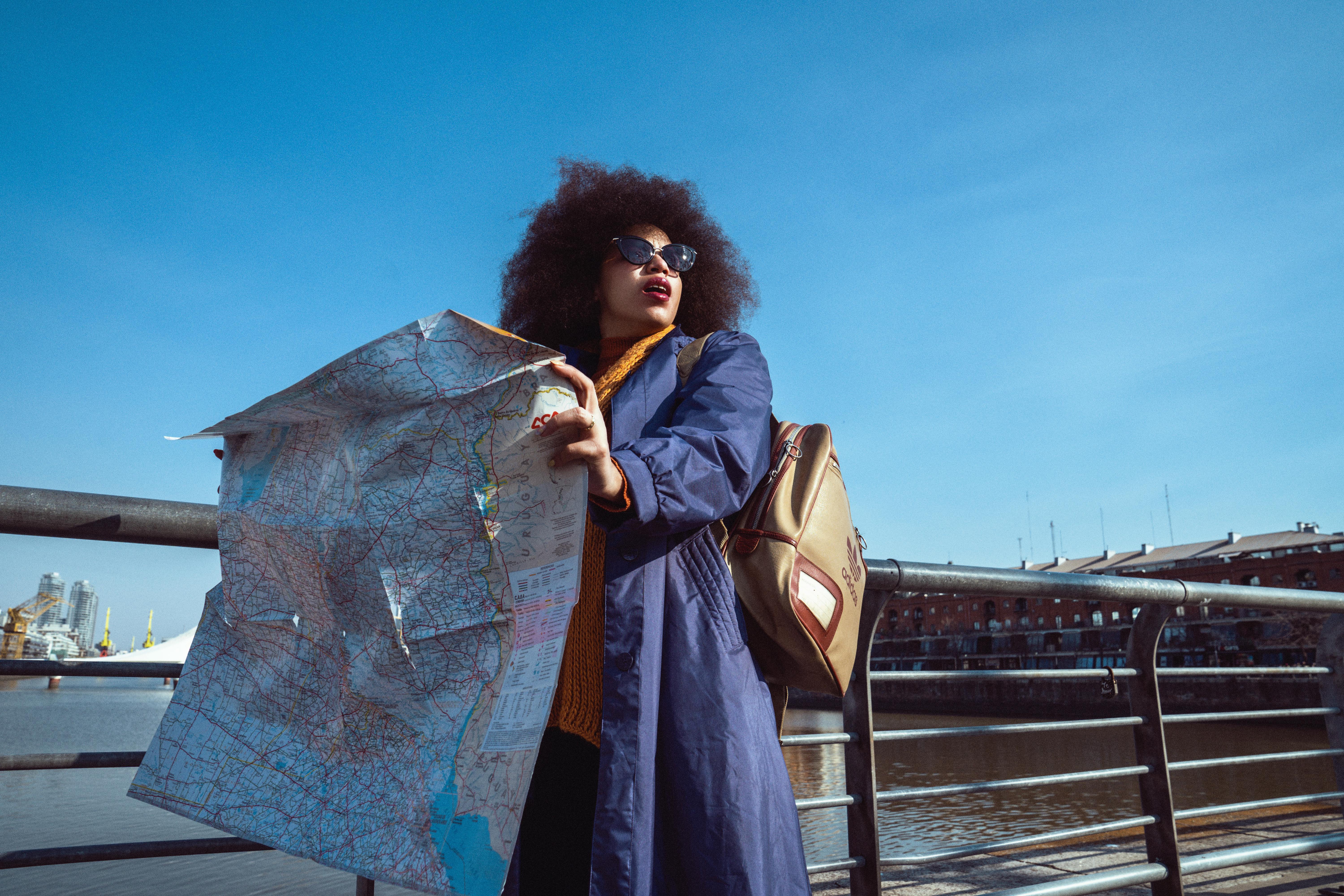 A young black woman looking for directions on a bridge, holding a large paper map.